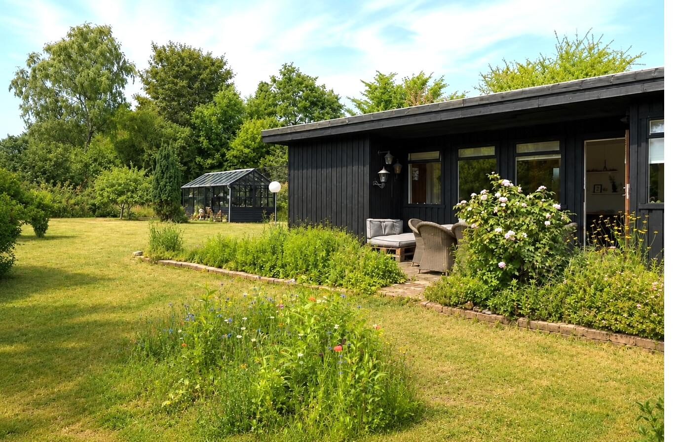 Sort træhus med orangeri set fra den vilde have – sommerhus til salg Nøddevej 9 Vejby Strand
