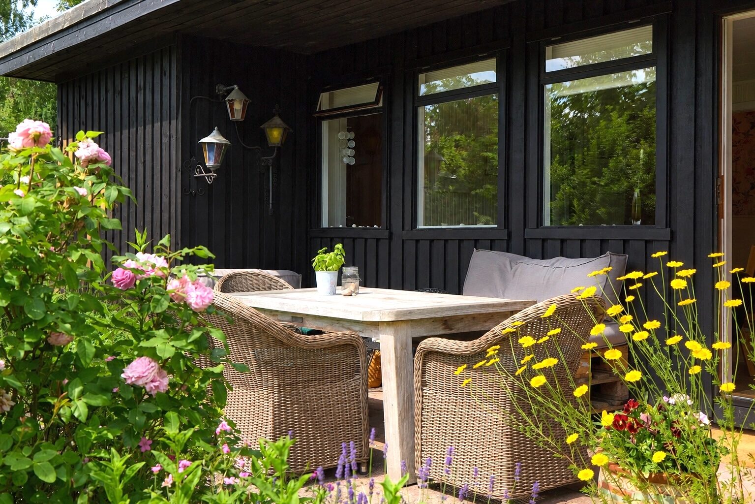 Terrasse med lanterner, roser og vilde blomster ved det sorte træhus – sommerhus Vejby Strand